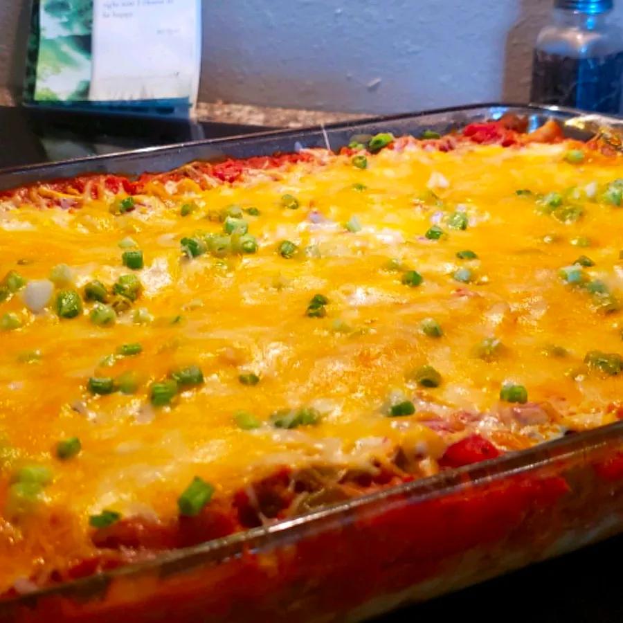 Mexican-style lasagna with layers of noodles, seasoned beef, refried beans, and bold spices, all topped with a rich blend of cheese and salsa for a comforting dish.